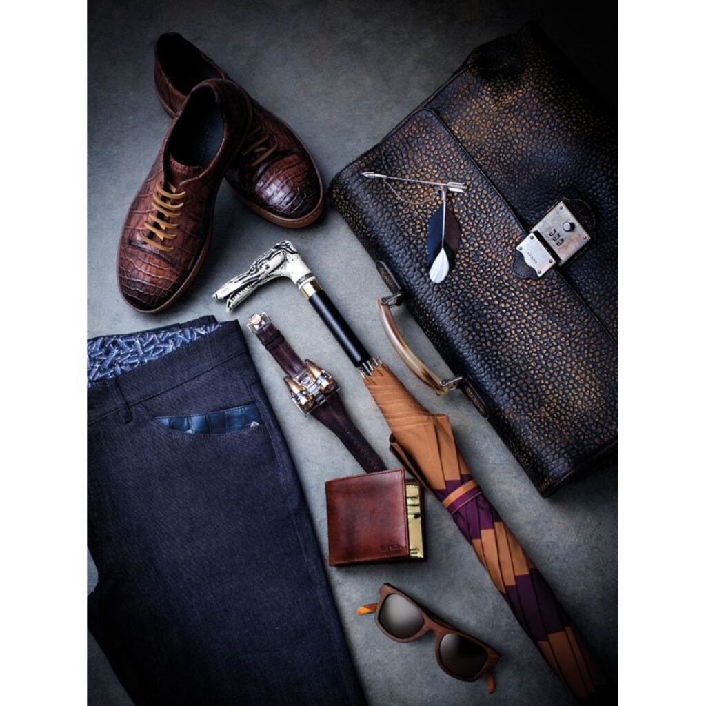 Αναδιάταξη από αξεσουάρ και ρούχα που περιλαμβάνει δερμάτινα παπούτσια, παντελόνι, τσάντα, πουγκί, ομπρέλα, ρολόι και γυαλιά ηλίου.